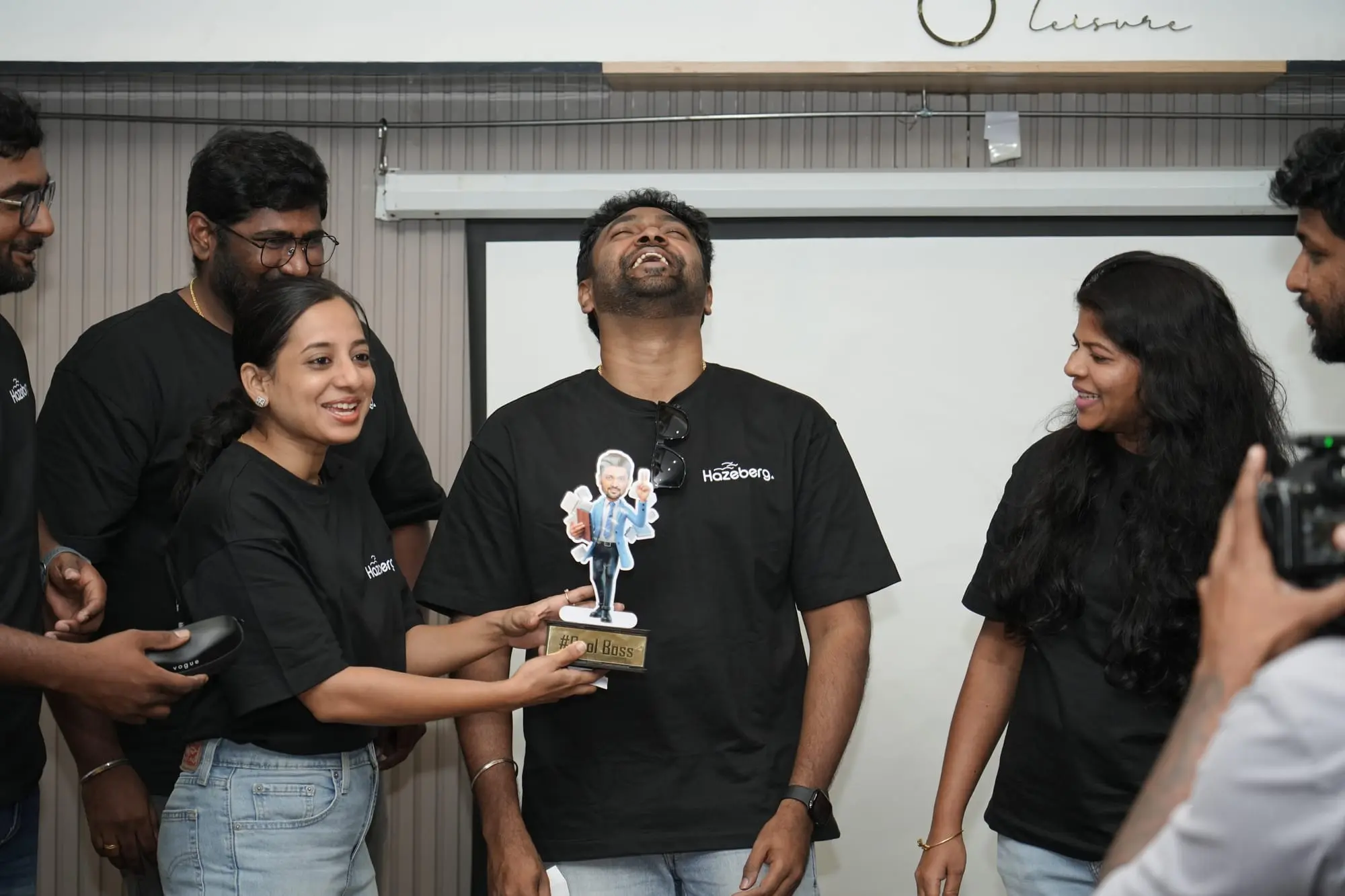 The team laughing as a colleague is handed a caricature trophy